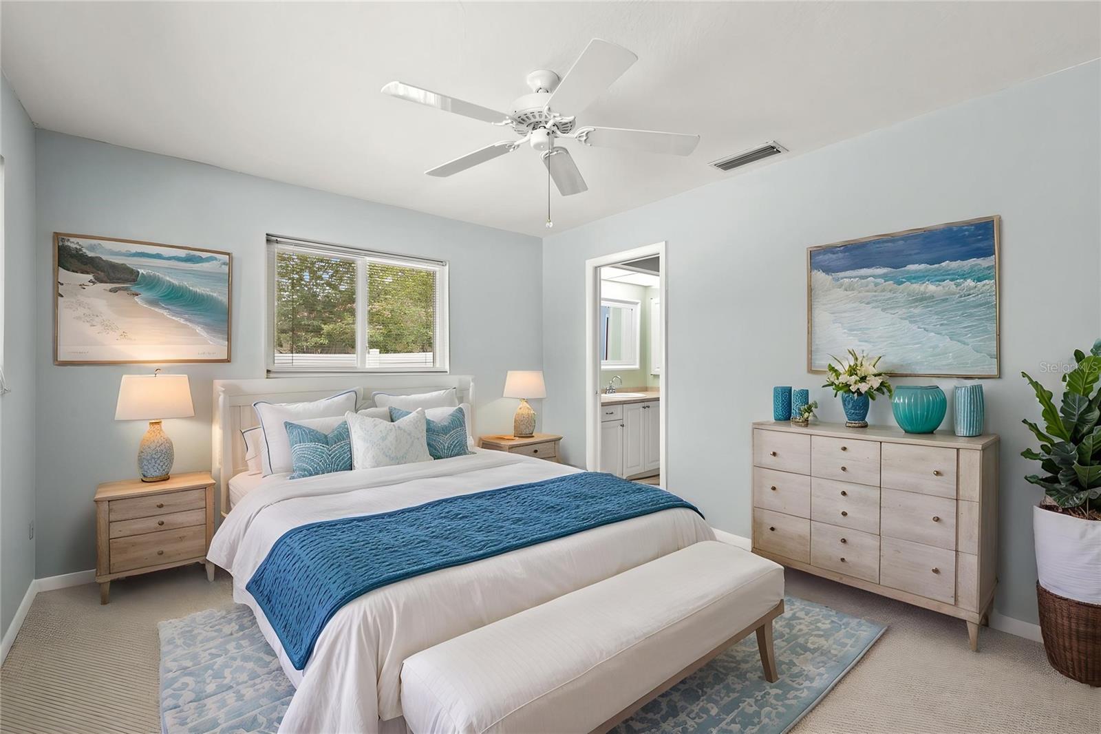 Soft blue walls and a ceiling fan set a calm, coastal tone in this bedroom, with a window bringing in natural light. A doorway leads directly to the adjoining Jack-and-Jill bathroom shared with the neighboring bedroom.