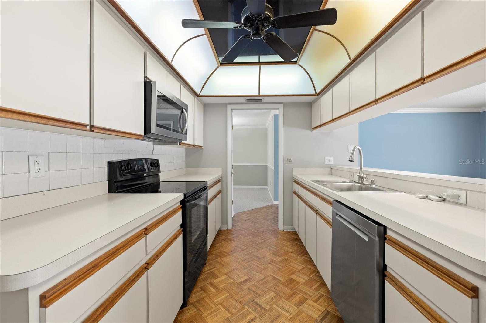 Rich wood-trimmed cabinetry and a domed skylight bring warmth and natural light into this galley-style kitchen, where black appliances and parquet flooring create a cohesive workspace.