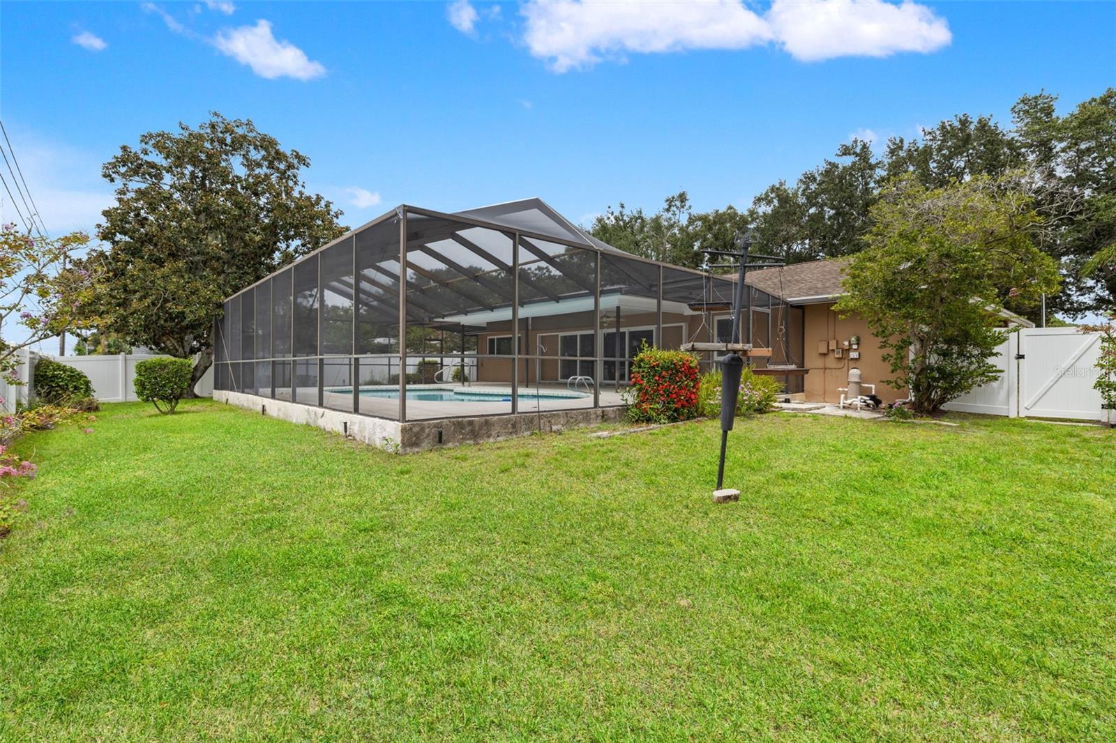 A sprawling lawn shaded by mature oak trees surrounds the screened pool enclosure, offering plenty of green space for play or relaxation beyond the water's edge.
