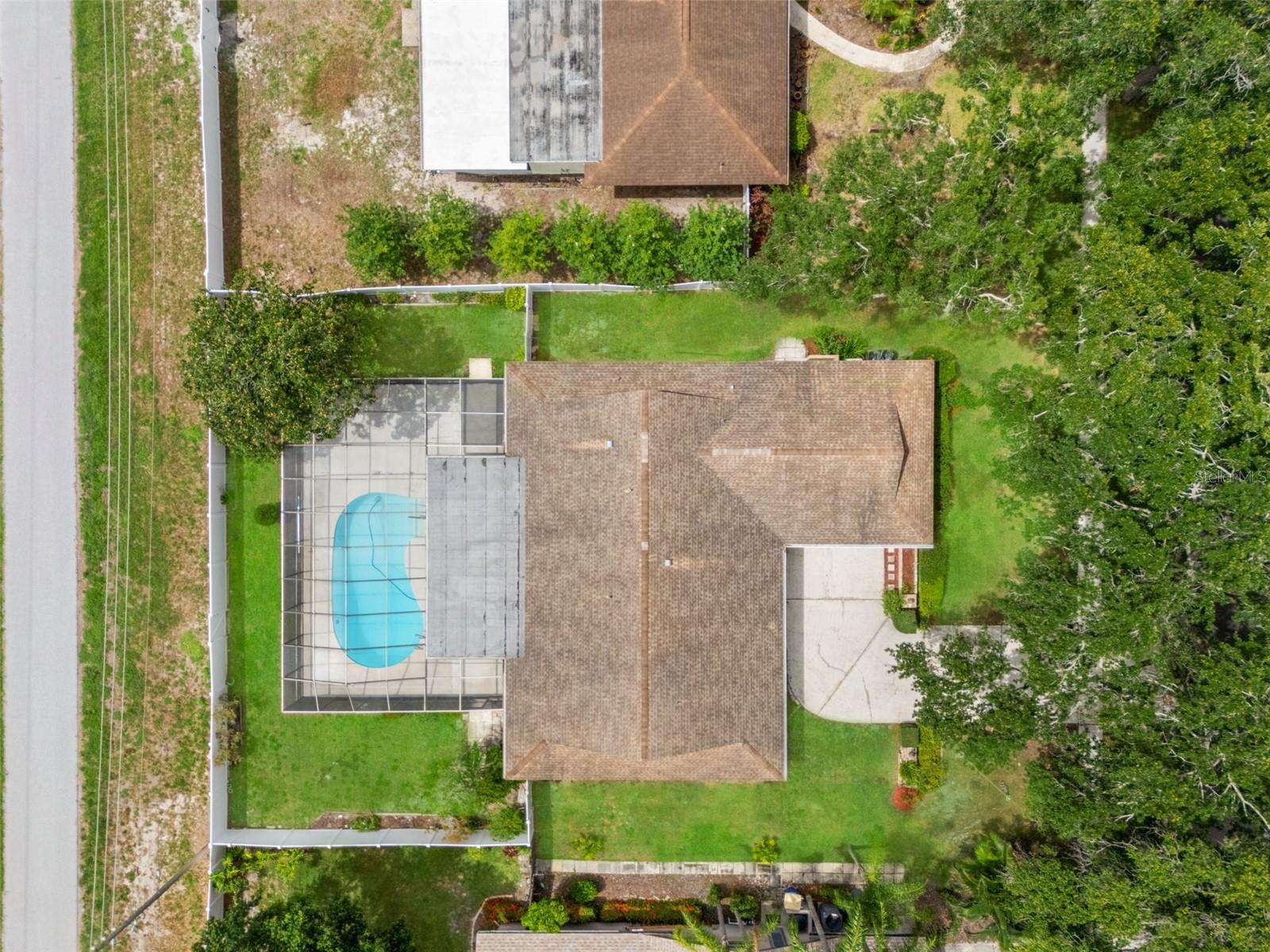 An aerial view captures the full scope of the property, with the screened pool, mature tree canopy, and fenced yard all visible in relation to the home.
