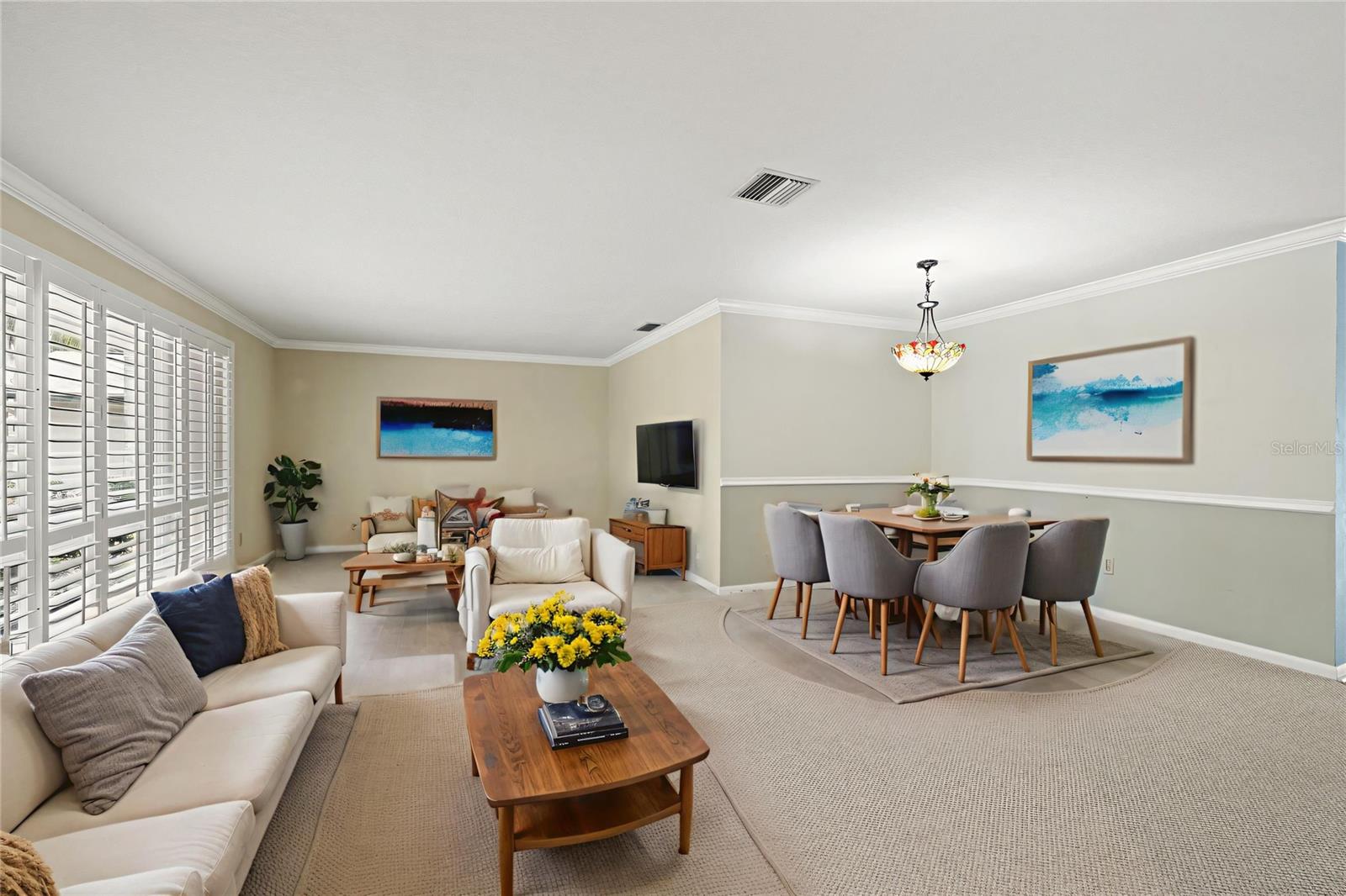 Light pours into this open living and dining space through a wall of windows, where a cream sectional and a round dining table create easy flow for relaxing and entertaining. Soft neutral tones and plush carpet give the room a calm, move-in-ready feel.