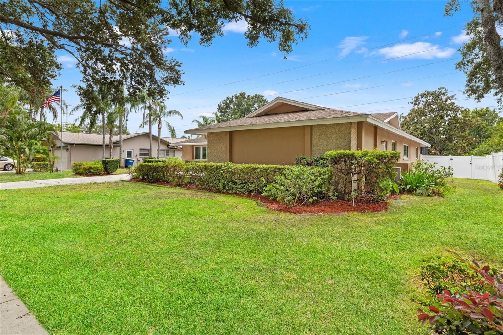 A wide view of the front exterior showcases the full width of the home alongside its landscaped lawn and long, tree-shaded driveway.