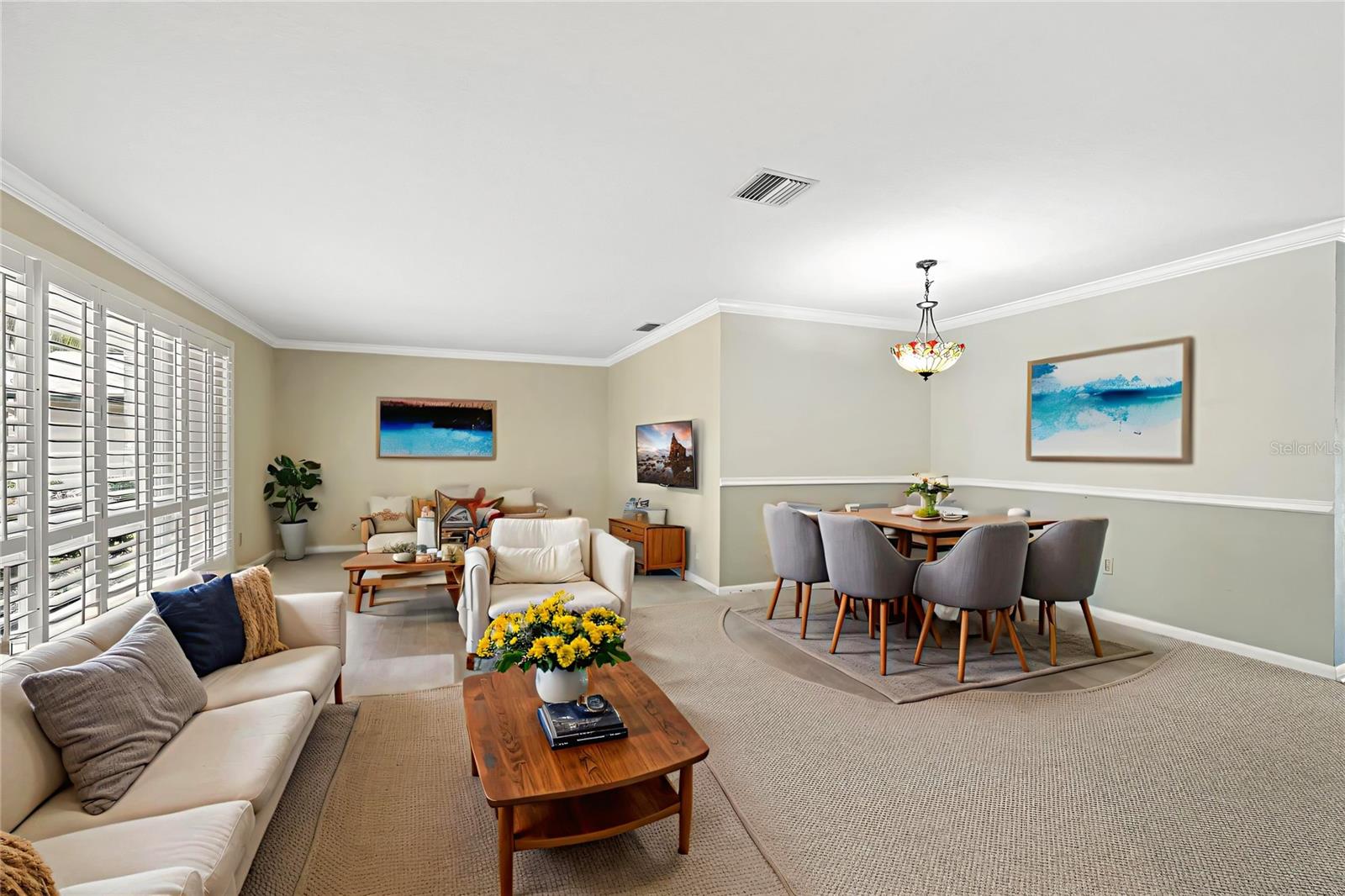 A wide view of the main living space shows how naturally the seating area flows into the dining table beyond, with coastal-inspired artwork and warm wood tones tying the room together.