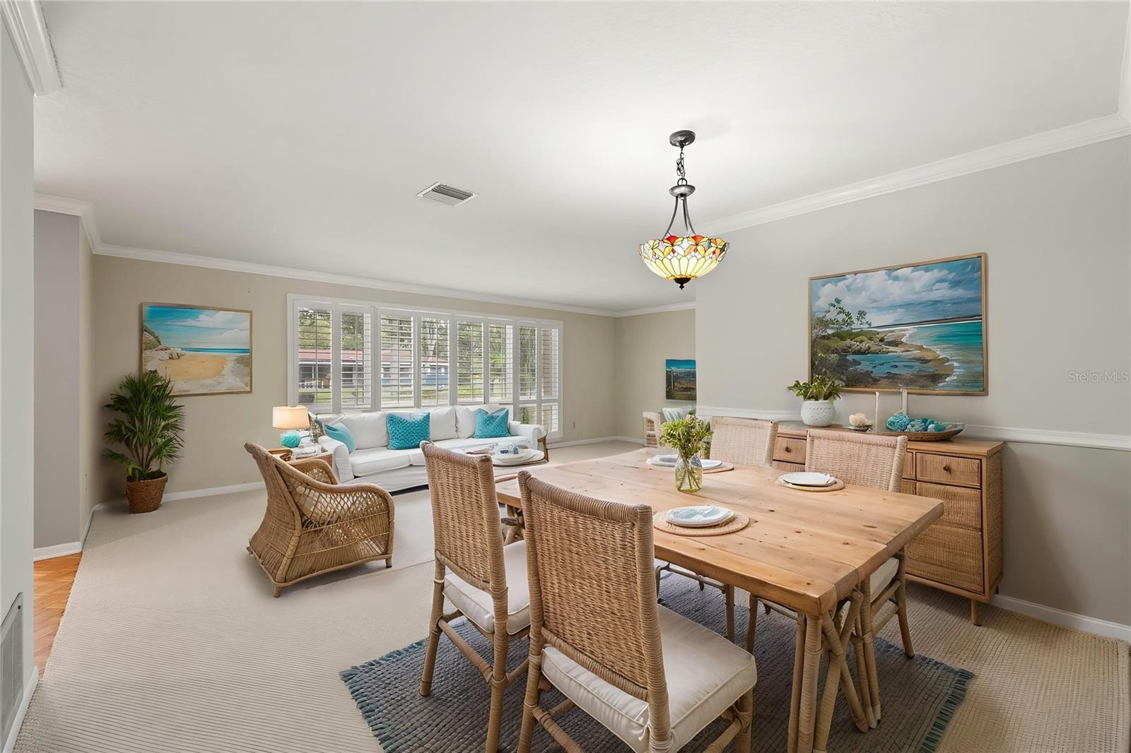 A reclaimed-wood dining table paired with woven wicker chairs creates a relaxed gathering spot just off the main living area, bathed in natural light from the surrounding windows.