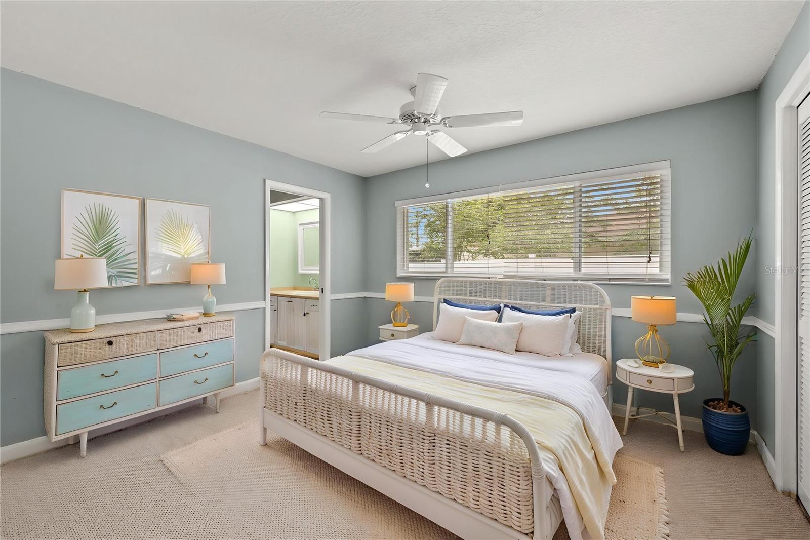 Soft blue walls and a white wicker bed frame give this secondary bedroom an airy, restful feel, with a ceiling fan and wall-to-wall carpet adding everyday comfort.