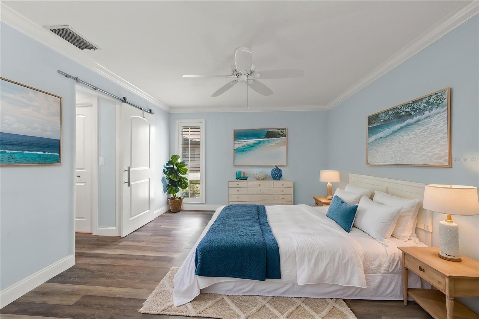 Wide-plank flooring and a deep blue accent wall lend a grounded, restful quality to the primary suite, while a sliding barn door adds a custom touch to the closet entry.