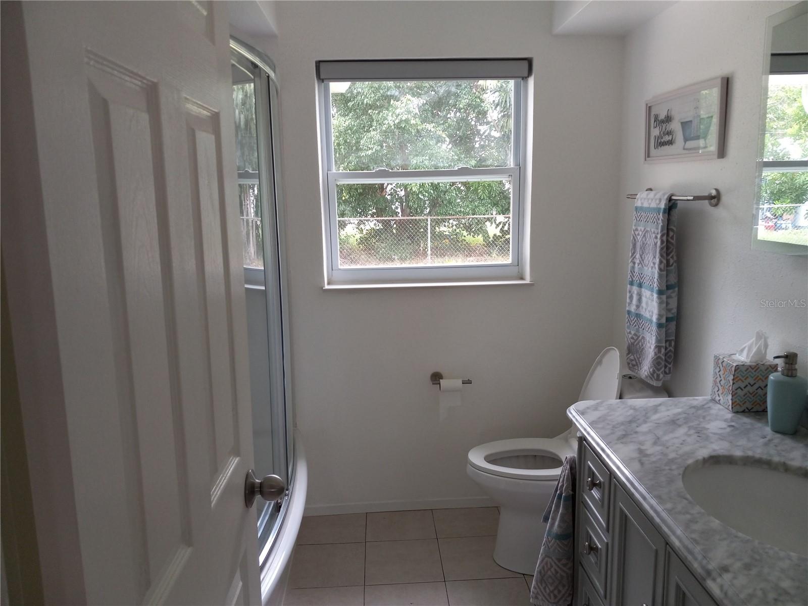 tastefully updated main bath, beautiful marble top vanity, bow front glass shower doors