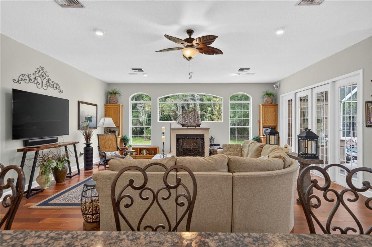 the impressive family room draws in the surrounding scenery through a striking arrangement of arched windows and multiple sets of French doors. Rich cherry wood floors and a gas fireplace bring warmth to this bright, open gathering space.