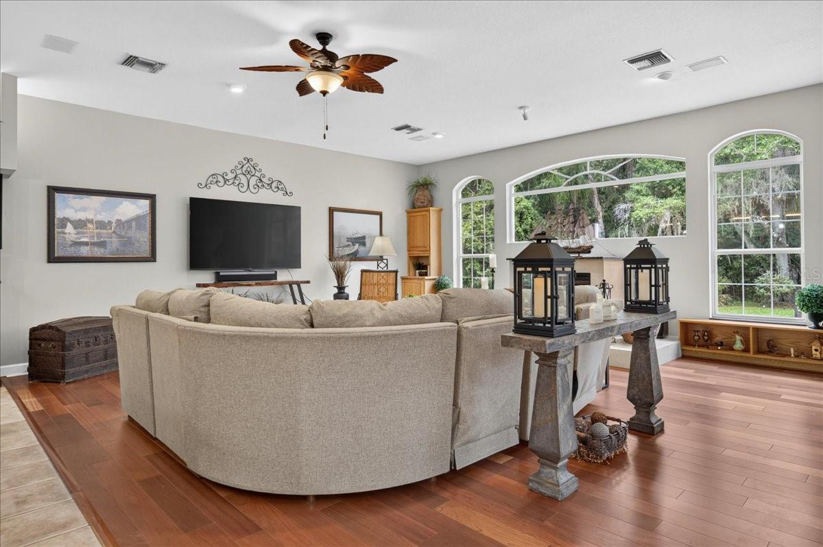the impressive family room draws in the surrounding scenery through a striking arrangement of arched windows and multiple sets of French doors. Rich cherry wood floors and a gas fireplace bring warmth to this bright, open gathering space.
