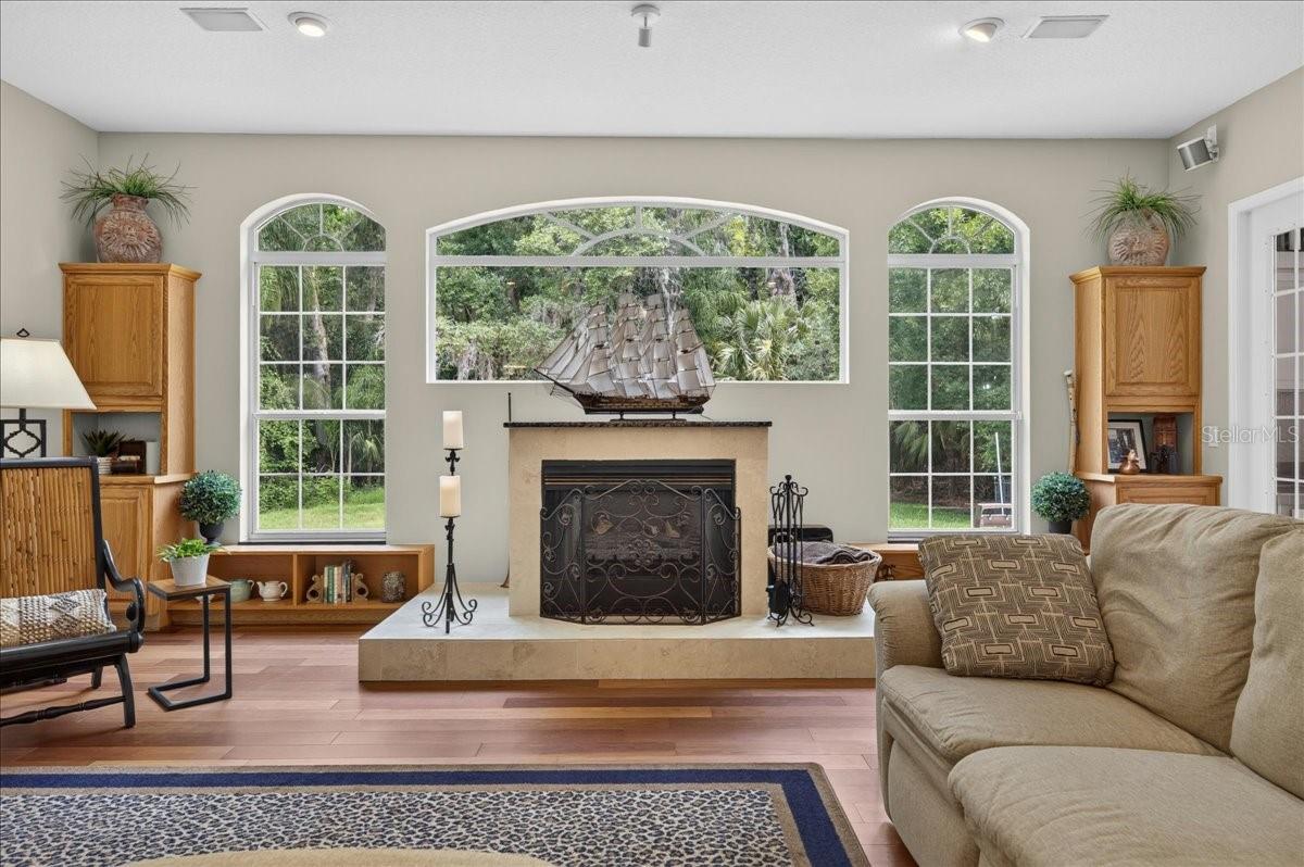 the impressive family room draws in the surrounding scenery through a striking arrangement of arched windows and multiple sets of French doors. Rich cherry wood floors and a gas fireplace bring warmth to this bright, open gathering space.