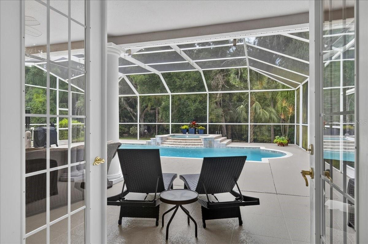 The primary bedroom retreat is set apart within the split-bedroom plan and features a transom window and French doors to the lanai and views beyond. Two walk-in closets with built-in organizers provide generous storage