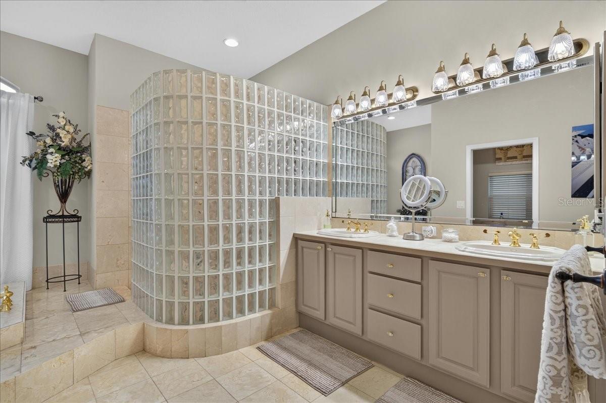 The ensuite bath offers extensive marble finishes, soaking tub, an oversized shower with a curved glass-block wall, double-sink vanity, and a separate water closet with bidet.