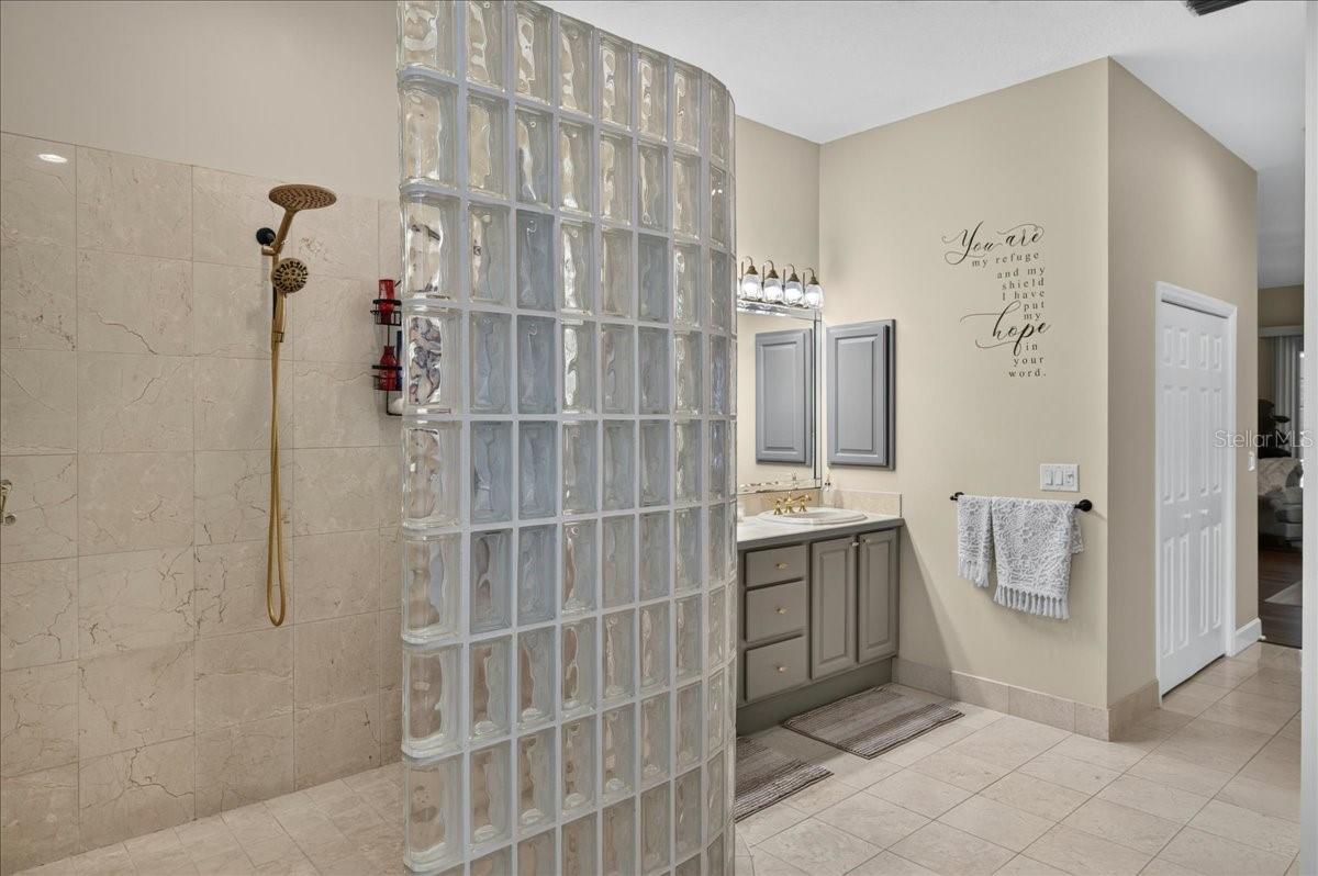The ensuite bath offers extensive marble finishes, soaking tub, an oversized shower with a curved glass-block wall, double-sink vanity, and a separate water closet with bidet.