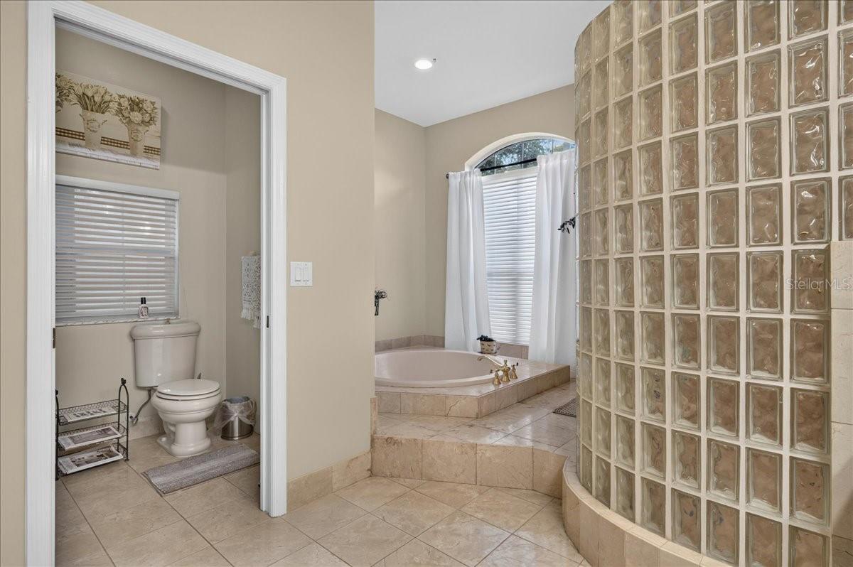 The ensuite bath offers extensive marble finishes, soaking tub, an oversized shower with a curved glass-block wall, double-sink vanity, and a separate water closet with bidet.