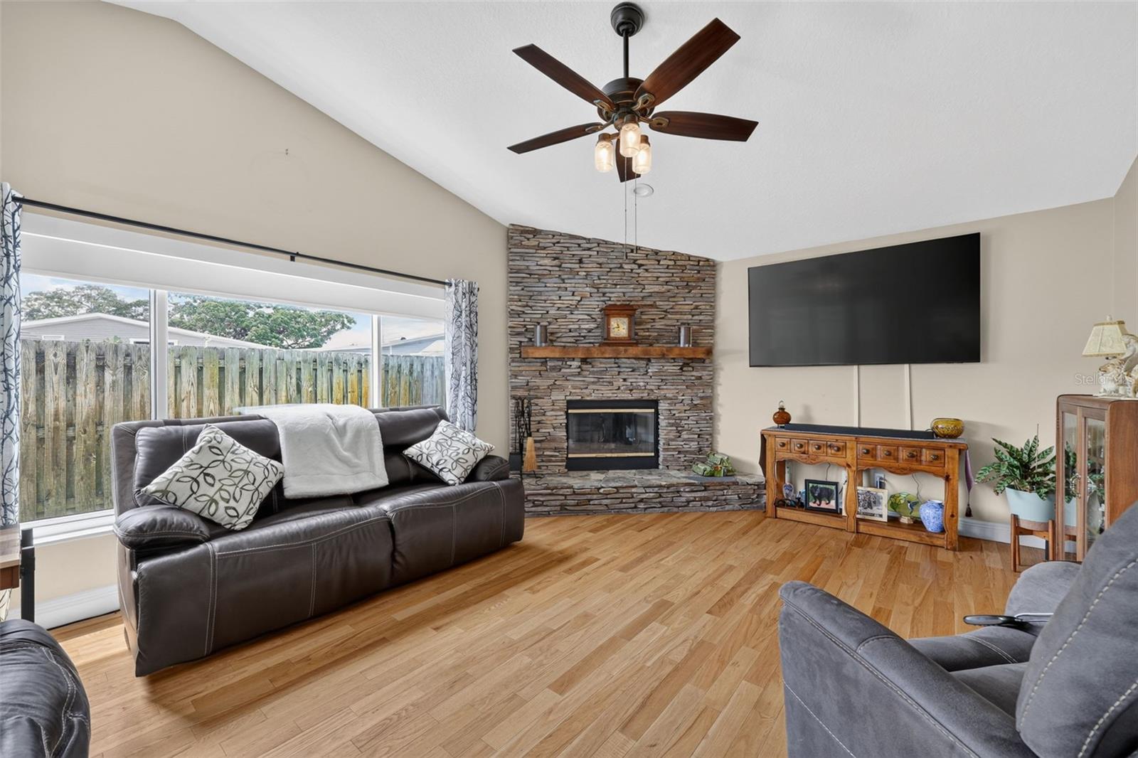 THe family room has a wood burning fireplace, ceiling fan and large picture window