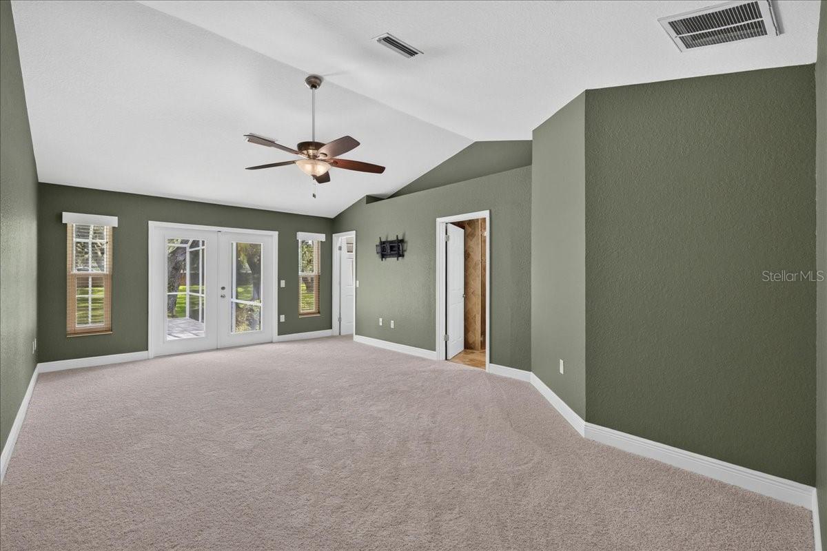 Vaulted ceilings continue into the primary bedroom, where French doors open to the pool and patio. A large walk-in closet and ensuite bath complete the space, with travertine flooring, a dual-sink granite vanity, jetted tub, separate walk-in shower and linen cabinetry.