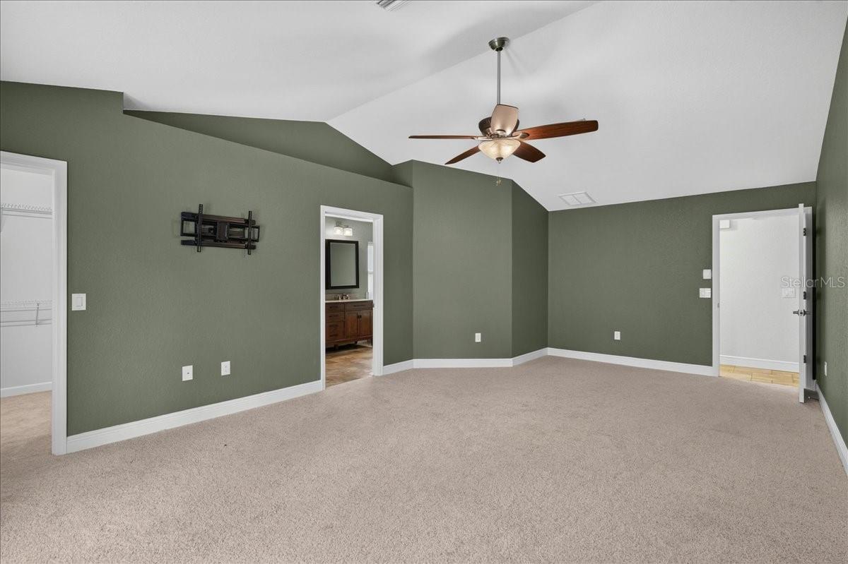 Vaulted ceilings continue into the primary bedroom, where French doors open to the pool and patio. A large walk-in closet and ensuite bath complete the space, with travertine flooring, a dual-sink granite vanity, jetted tub, separate walk-in shower and linen cabinetry.