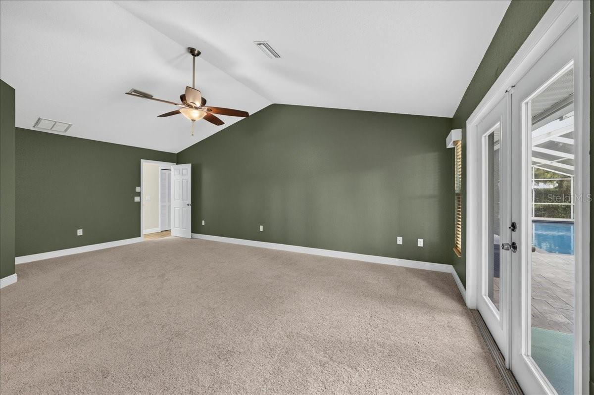 Vaulted ceilings continue into the primary bedroom, where French doors open to the pool and patio. A large walk-in closet and ensuite bath complete the space, with travertine flooring, a dual-sink granite vanity, jetted tub, separate walk-in shower and linen cabinetry.