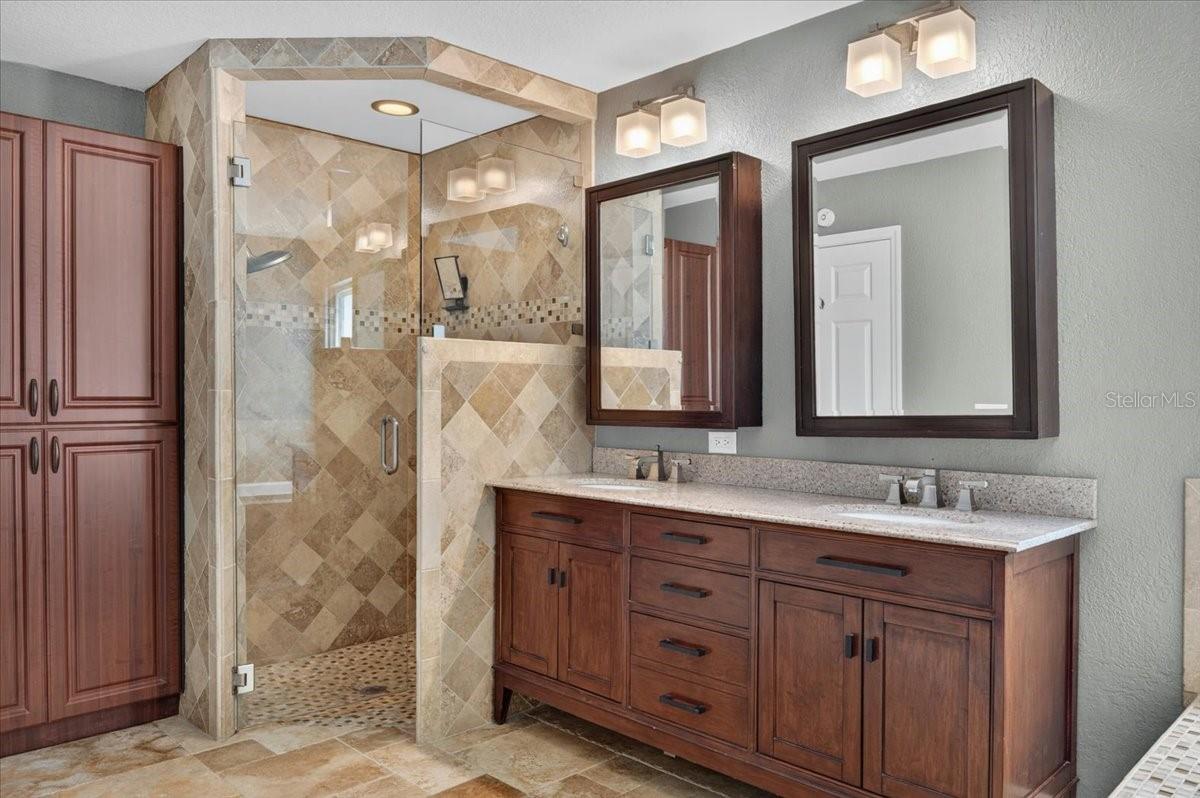 The ensuite bath features travertine flooring, a dual-sink granite vanity, jetted tub, separate walk-in shower, and built-in cabinetry for linens and additional storage.