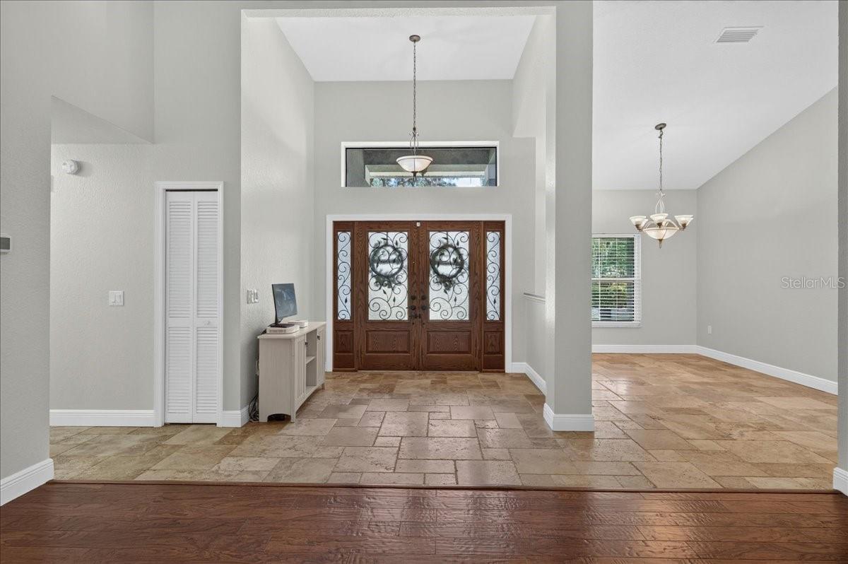 Double glass-and-wrought-iron entry doors, accented by sidelights and a transom window, open to a bright interior where travertine flooring flows through the foyer, formal dining room and kitchen.
