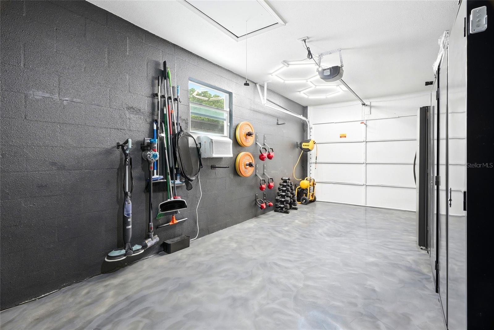 Immaculate garage with a finished epoxy floor, A/C unit, double utility sink, and pull down attic stairs