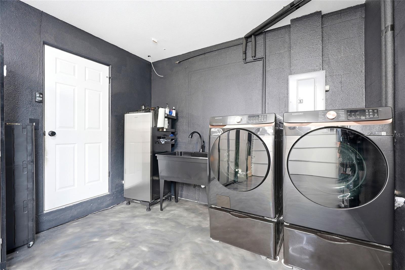 Immaculate garage with a finished epoxy floor, A/C unit, double utility sink, and pull down attic stairs