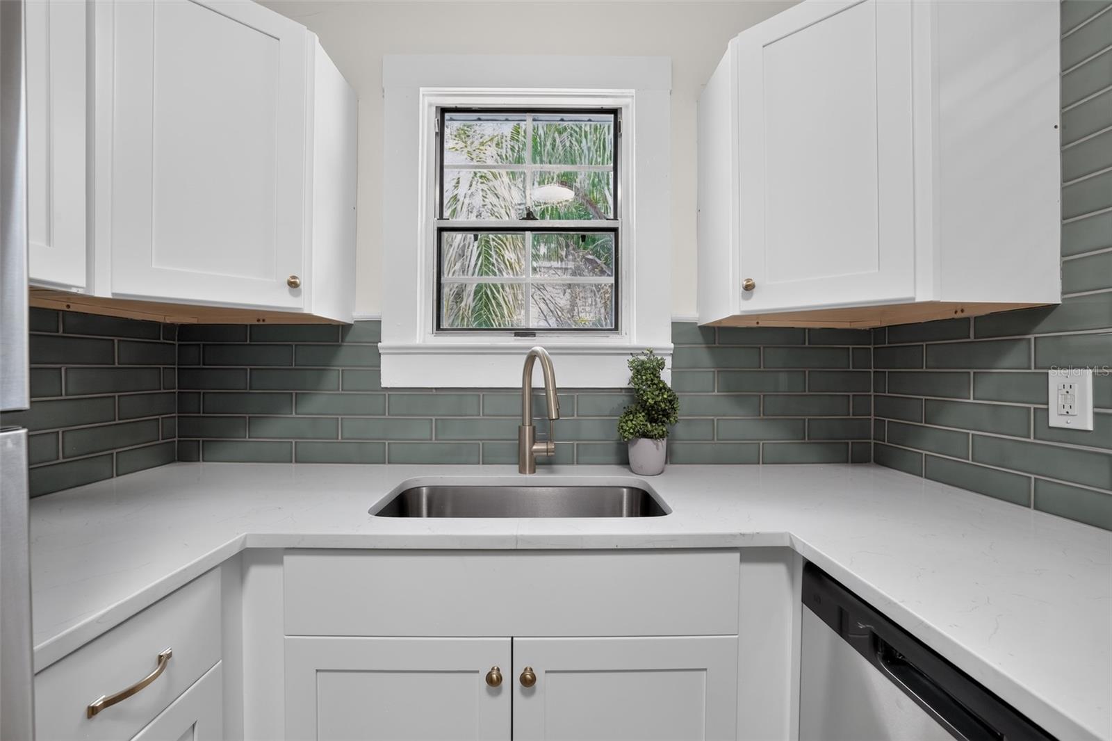 Bright kitchen sink area with quartz counters and soft green tile in this 1922 bungalow