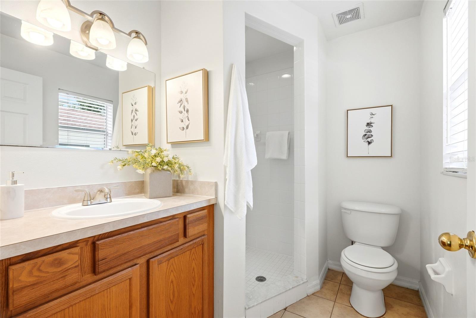 Primary bathroom has solid wood cabinetry and walk in shower with white square tile.