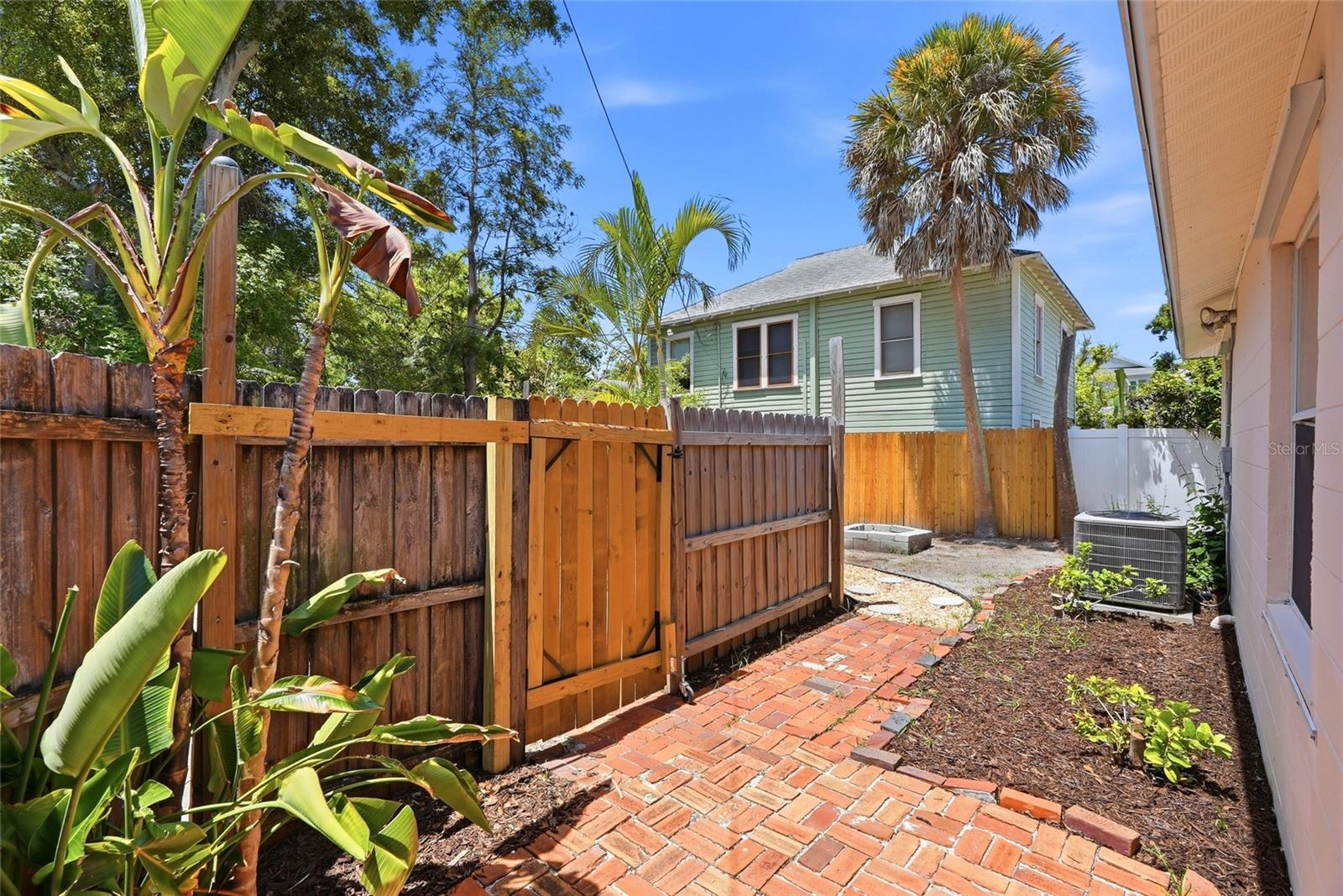 Reclaimed brick pavers wind through tropical greenery to a fenced side yard — a charming nod to the neighborhood's historic brick streets.