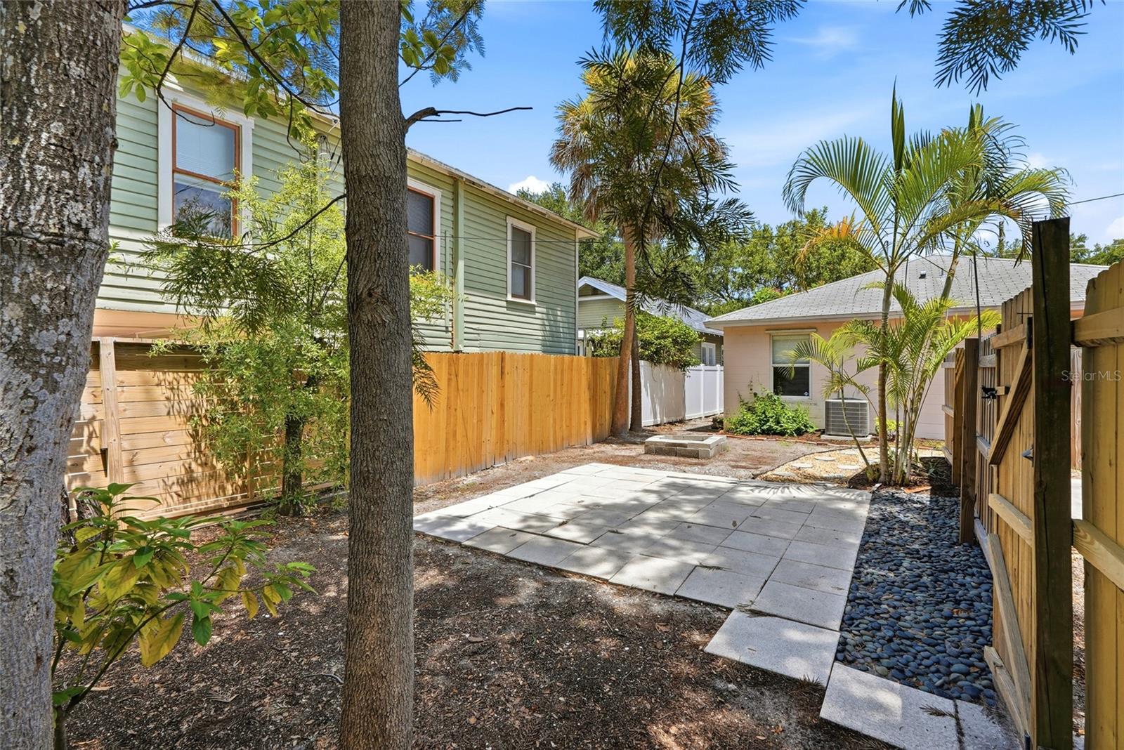 Part of the yard gets shade from mature palms and trees, with a paved patio area ready for outdoor furniture, string lights, or a cozy seating nook.