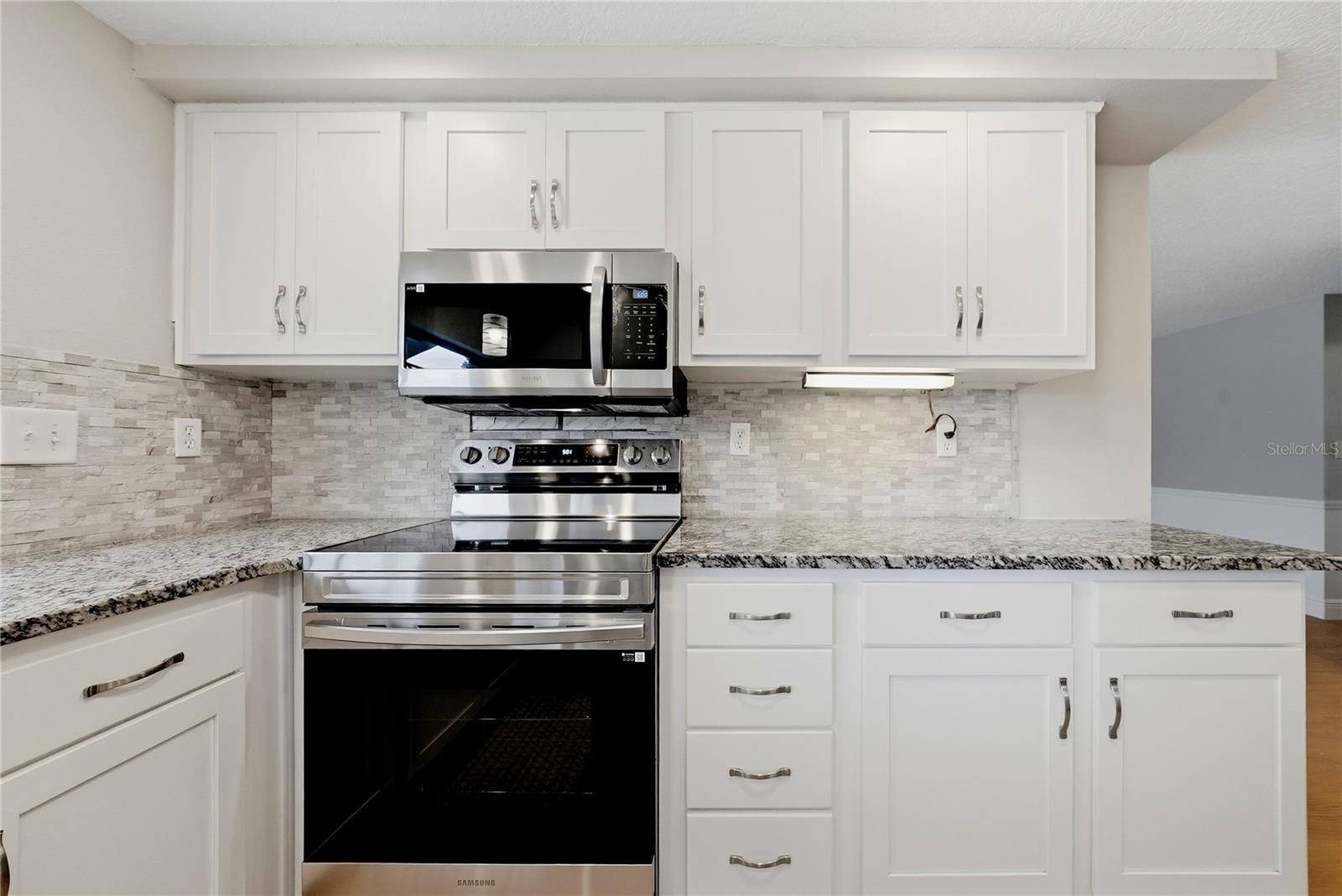 Updated cooking area featuring stainless-steel appliances, granite countertops, tile backsplash, and plentiful cabinetry.
