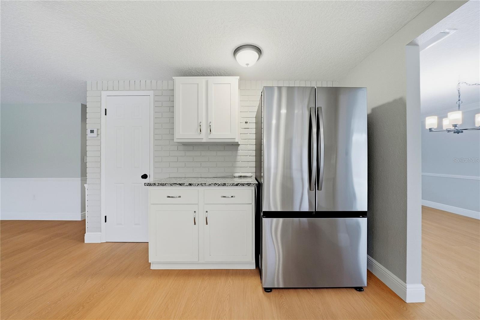Stainless-steel refrigerator, additional cabinetry, granite serving counter, and convenient pantry access.