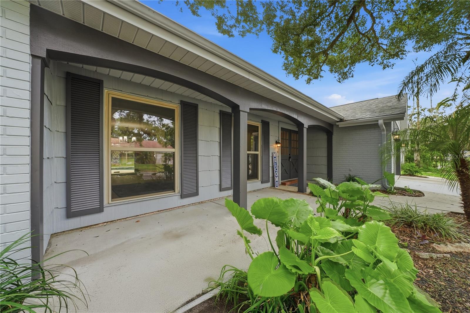 Generous covered front porch framed by tropical landscaping and large windows that bring natural light indoors.