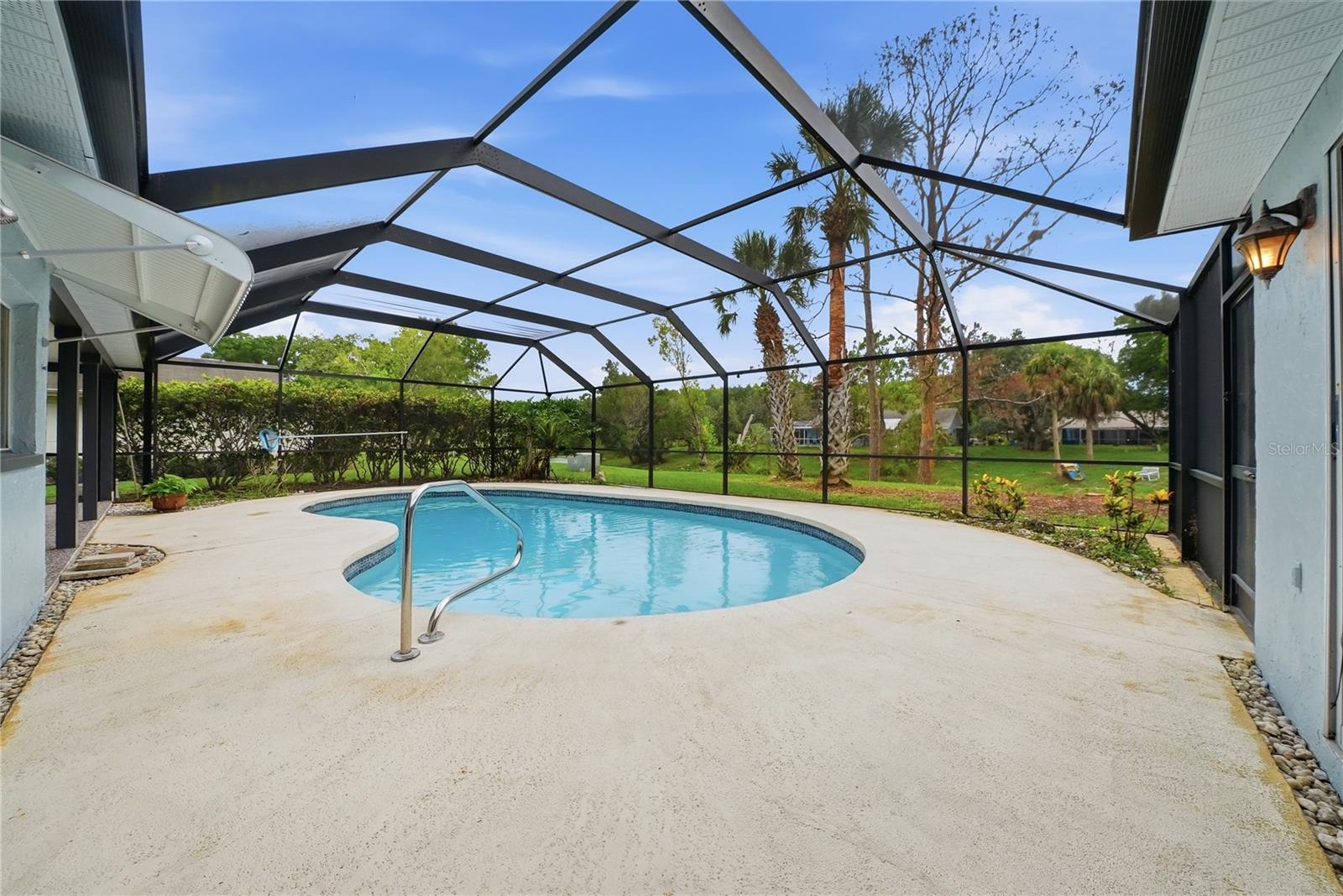 Peaceful poolside view overlooking the green backyard and waterfront setting beyond.