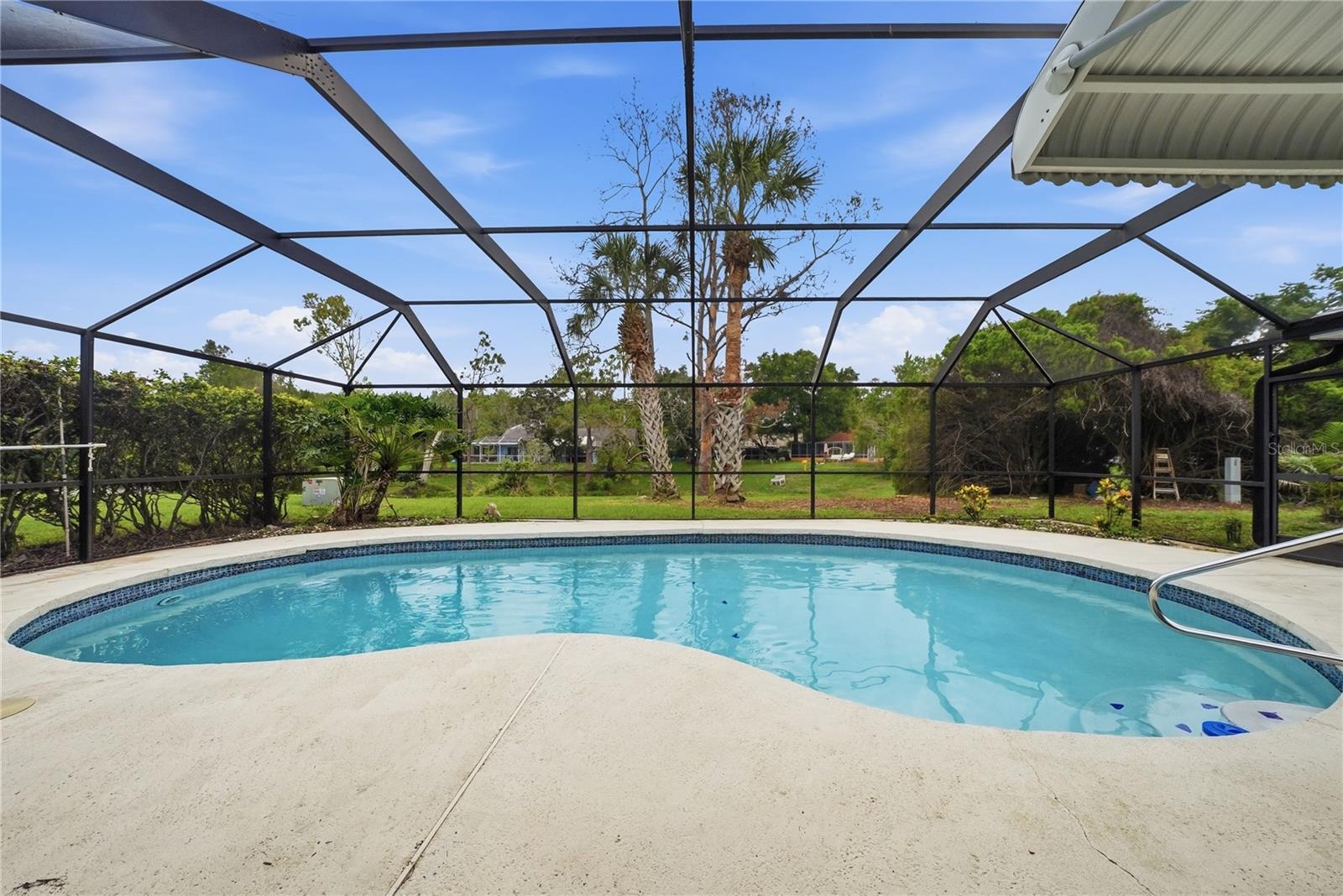 Wide poolside view showcasing the spacious deck, screened enclosure, and tranquil natural backdrop.