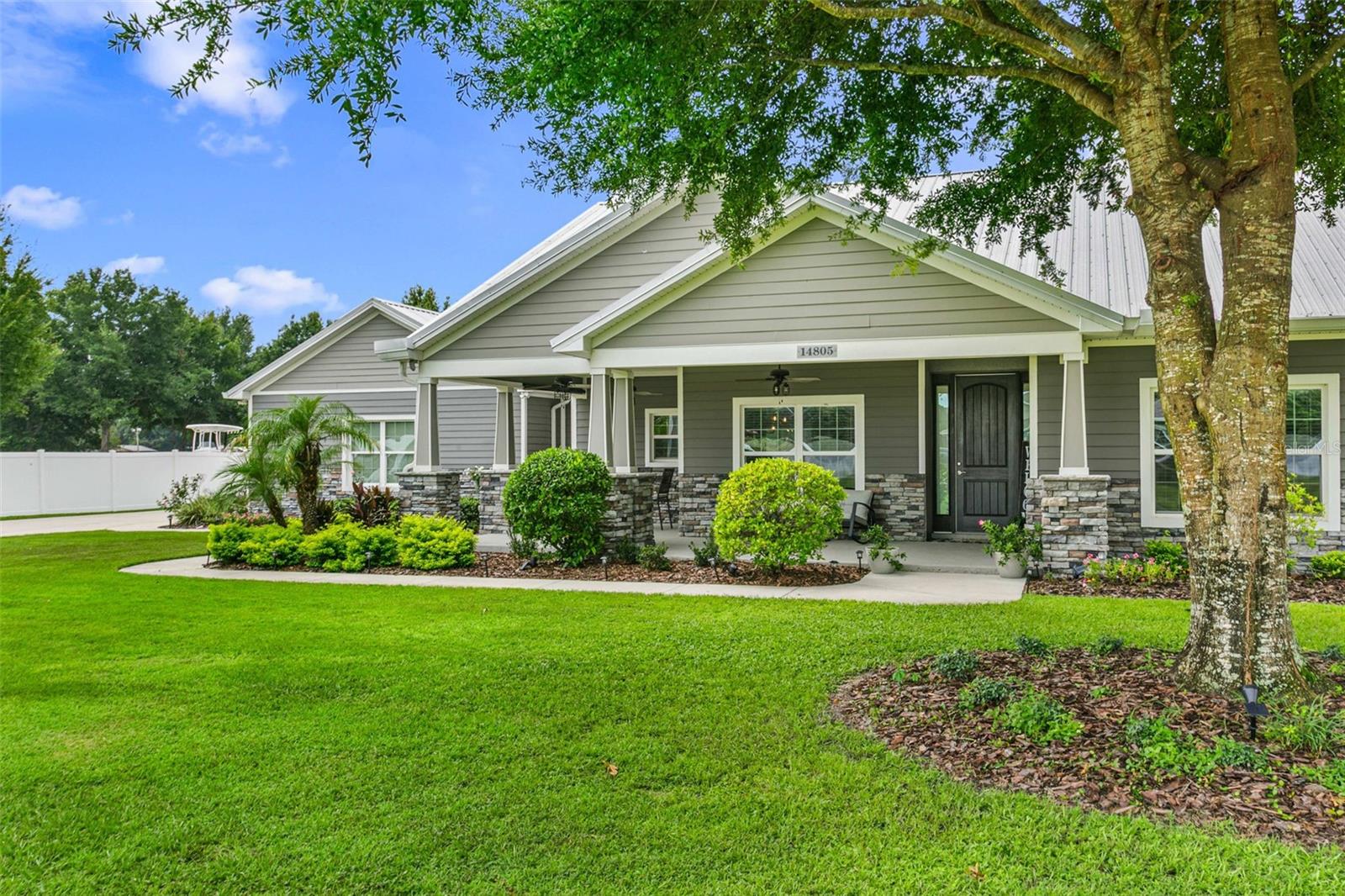 Beautiful angled view highlighting the home's charming covered front porch, mature oak trees, manicured landscaping, and timeless curb appeal on an expansive homesite.